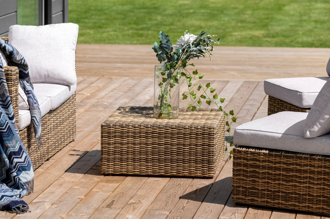 Gartenlounge aus Rattan mit gemütlichen Polstern und dekorativem Beistelltisch auf einer Holzterrasse im Sommer