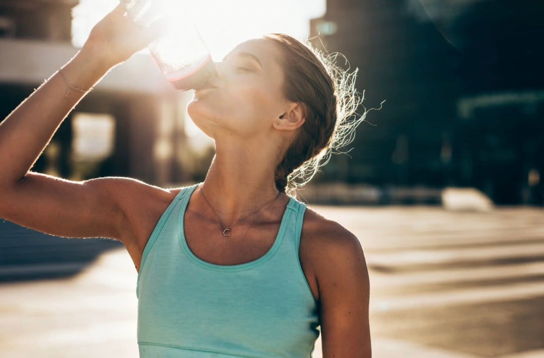 Frau trinkt unterwegs aus Trinkbecher in der Sonne – Hydration und Sommer Essentials für heisse Tage