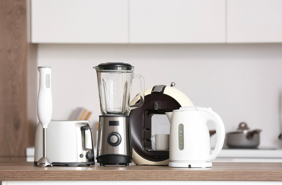 Moderne Küchengeräte wie Blender, Wasserkocher, Toaster und Stabmixer auf Holzarbeitsfläche in heller Küche.