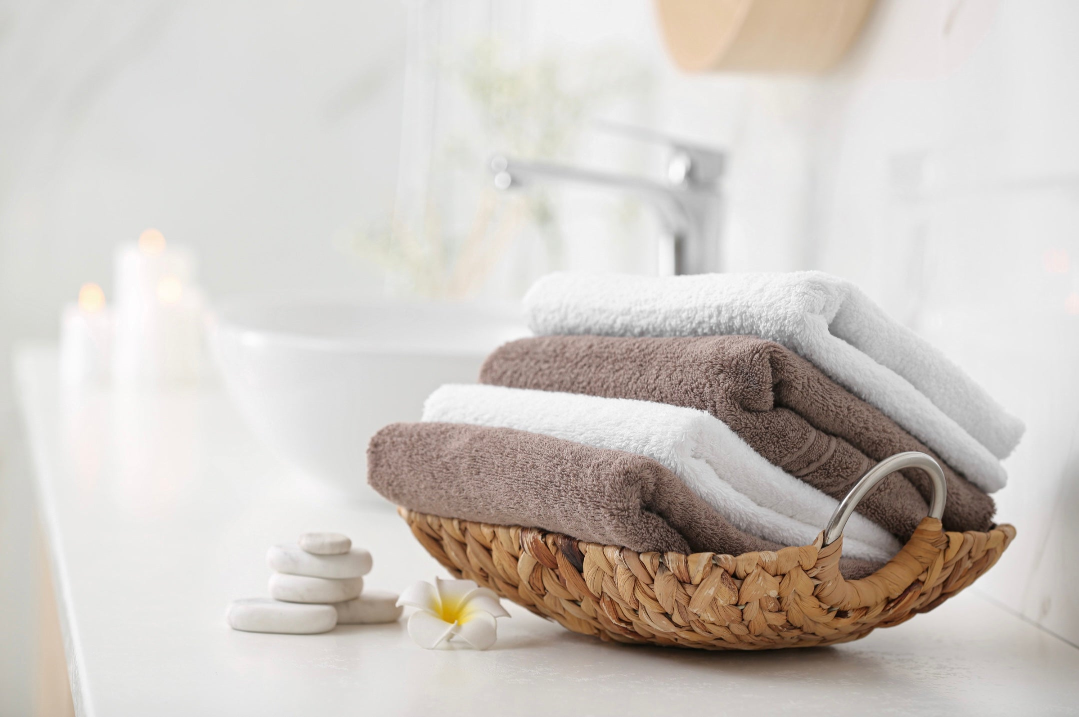 Gefaltete Baumwoll-Handtücher in Naturfarben im geflochtenen Korb, dekorativ im Badezimmer platziert – hochwertige Badtextilien für Wellness und Spa.