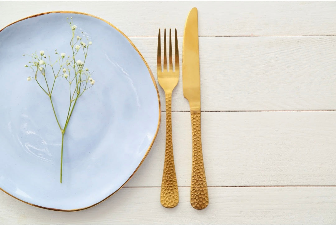 Stilvolles Gedeck mit goldenem Besteck und hellblauem Teller auf hellem Holztisch