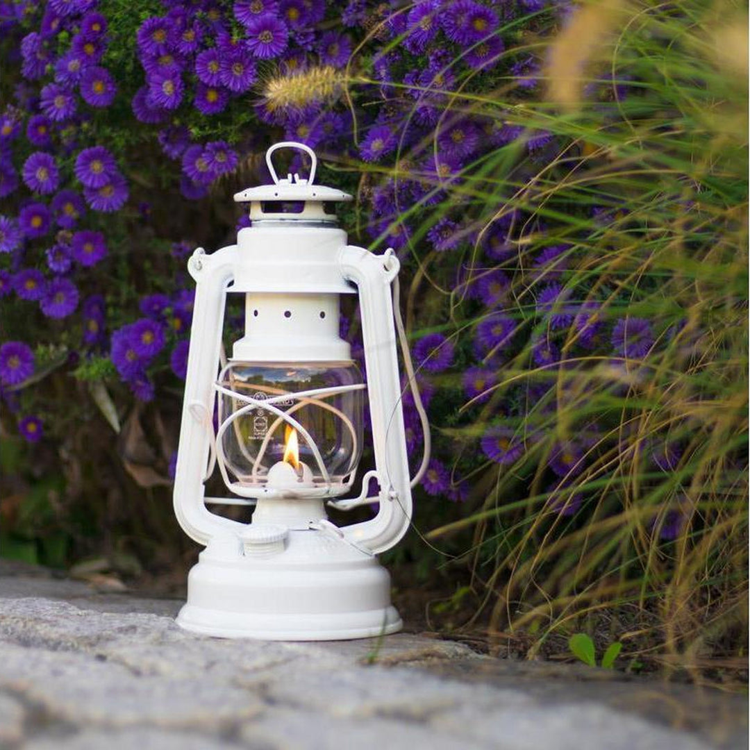 Feuerhand Sturmlaterne Baby Special 276, Pure White auf Steinplatte vor Blumen