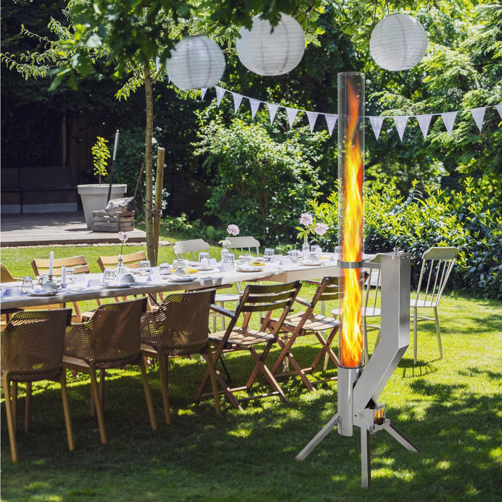 Gardenflare Premium Feuerrohr Edelstahl, brennend im Garten neben einer gedeckten Tafel