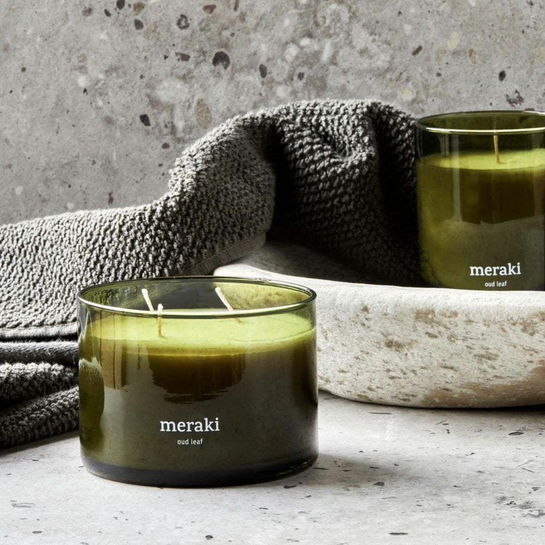 Meraki Duftkerze Oud Leaf, auf Stein neben grauem Frottiertuch