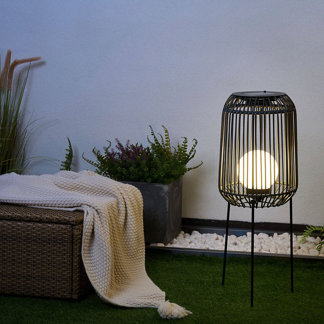 Beleuchtete Solar-Stehleuchte im Garten neben Rattanbox mit Strickdecke