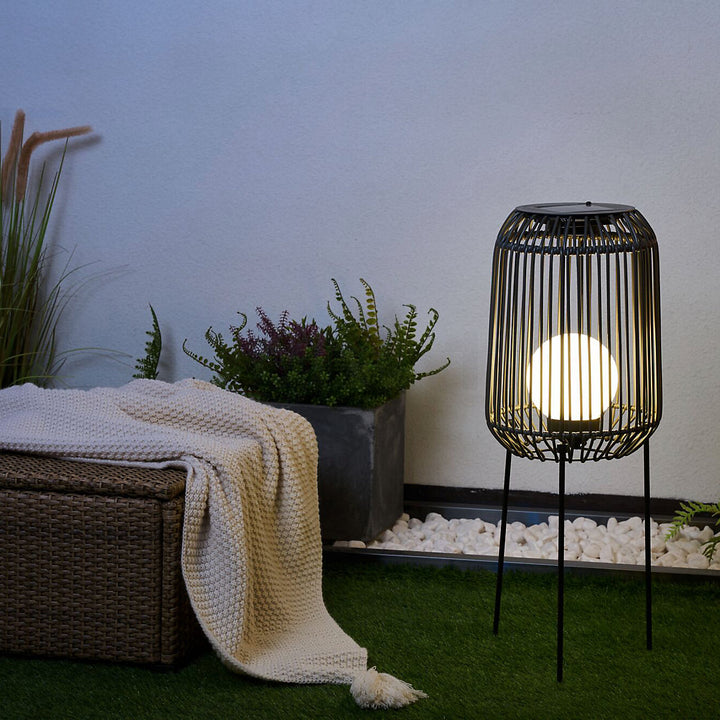 Beleuchtete Solar-Stehleuchte im Garten neben Rattanbox mit Strickdecke
