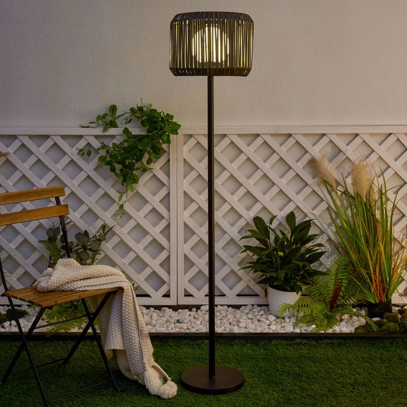 Solar-Stehleuchte am Abend auf Rasen neben Gartenstuhl und Pflanzen