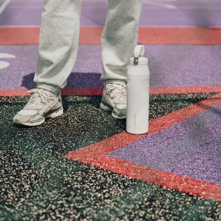 Weisse Stanley IceFlow auf dem Boden eines Sportplatzes neben Turnschuhen