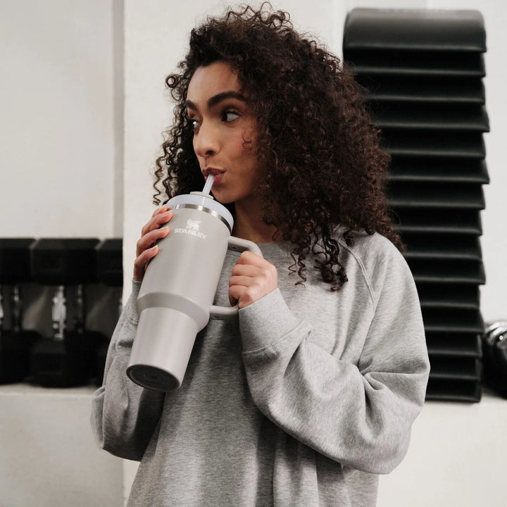 Frau trinkt im Fitnessstudio aus dem Stanley Quencher H2.0 in Grau